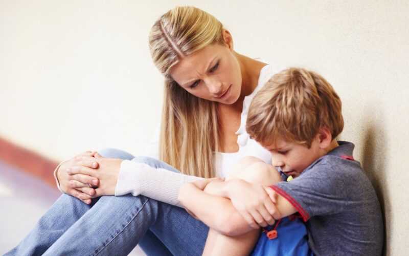 vrouw naast jongen die tegen de muur op een gang zit