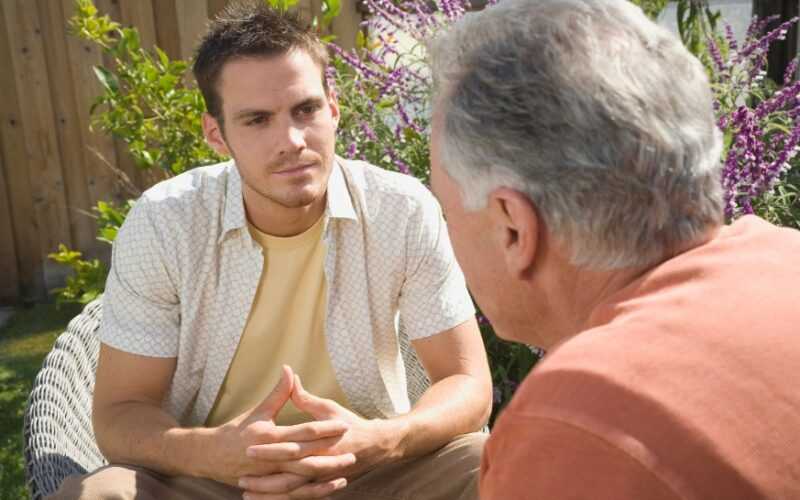 oudere en jongere man in gesprek zittend in de tuin